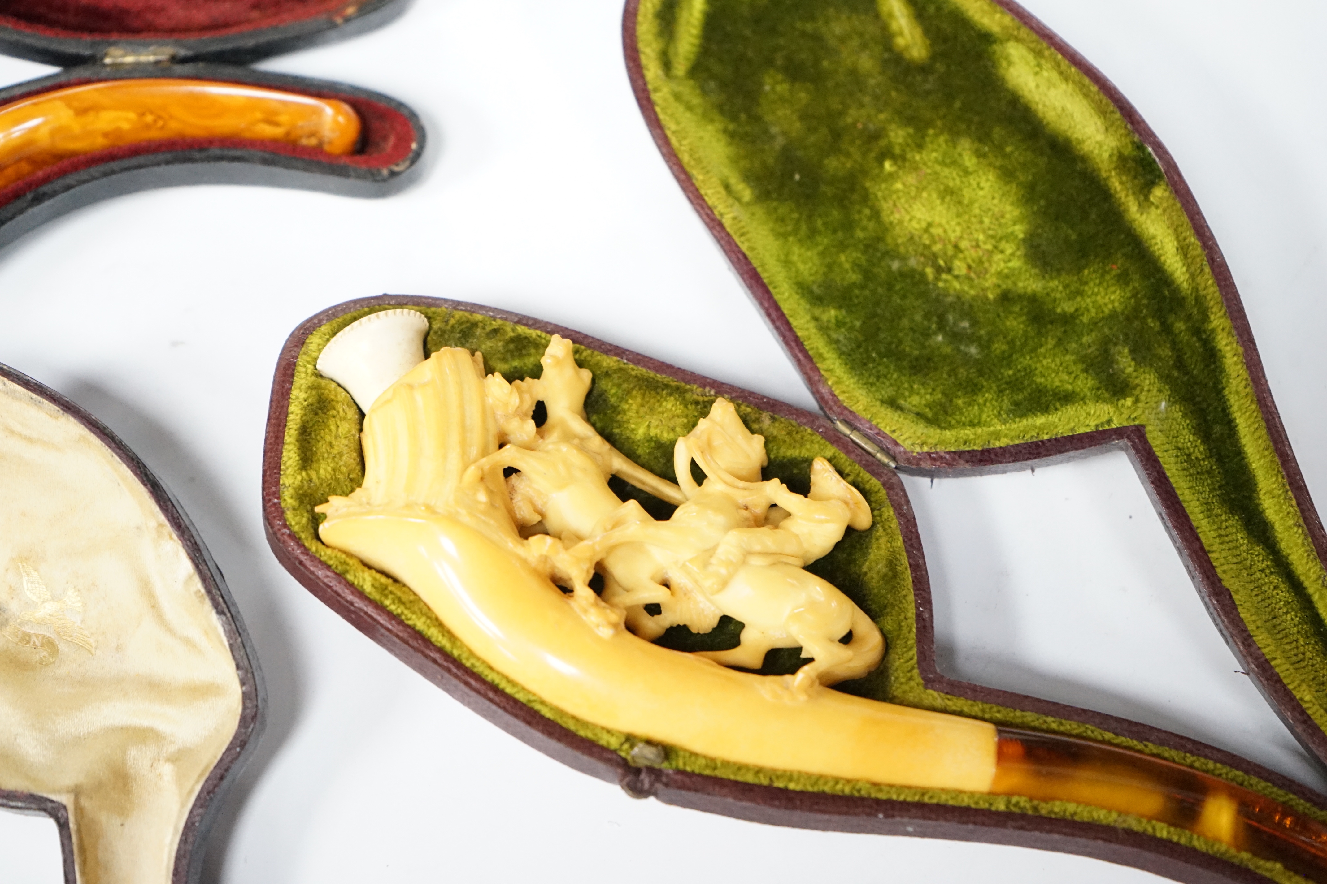 Three cased novelty Meerschaum pipes and pipe bowls, all with amber mouth pieces, one of a horses and cowboy, another a model of a hand and the other of a scantily clad lady wearing a riding cap, largest 17 cm long